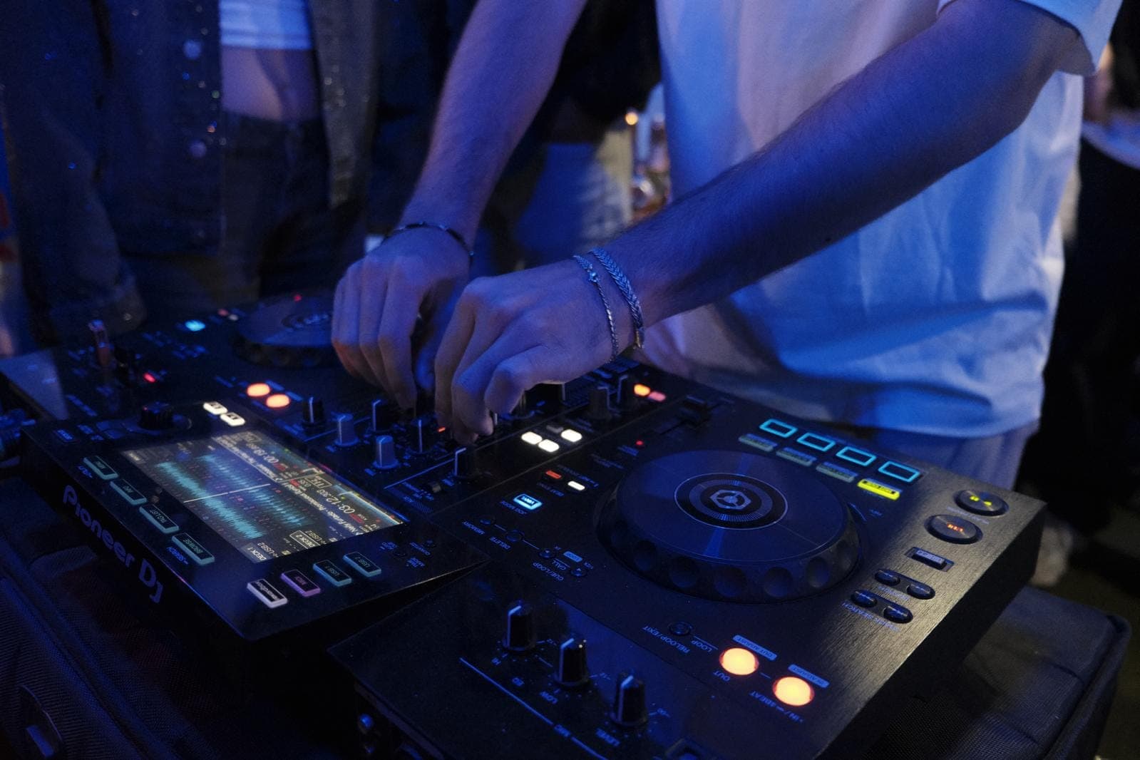 Mavi ışık altında bir DJ'in elleri, kontrol cihazının mikser düğmelerinde